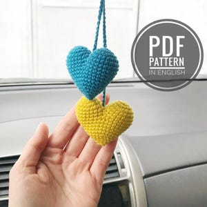 May include: Two crocheted hearts, one blue and one yellow, hanging from a rearview mirror.  PDF PATTERN IN ENGLISH.