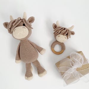 Puede incluir: Dos juguetes de vaca Highland de crochet en marr&oacute;n y blanco. El juguete m&aacute;s grande es un juguete de peluche y el juguete m&aacute;s peque&ntilde;o es un sonajero con un anillo de madera.