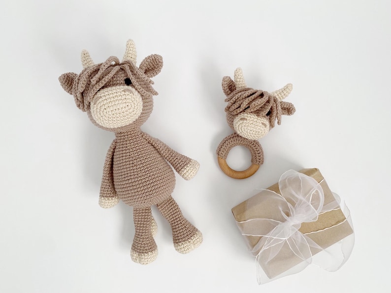 Puede incluir: Dos juguetes de vaca Highland de crochet en marr&oacute;n y blanco. El juguete m&aacute;s grande es un juguete de peluche y el juguete m&aacute;s peque&ntilde;o es un sonajero con un anillo de madera.