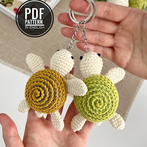 Puede incluir: Dos llaveros de tortuga hechos a mano con ganchillo. Una tortuga tiene un caparaz&oacute;n amarillo y azul, la otra tiene un caparaz&oacute;n verde. Ambas tortugas tienen cabezas y extremidades de color blanquecino. Los llaveros est&aacute;n sujetos por una cadena y un anillo plateados. El texto "PDF PATTERN IN ENGLISH".
