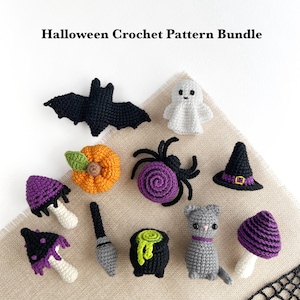 Puede incluir: Una colección de pequeños objetos de ganchillo de Halloween que incluye un murciélago negro, un fantasma blanco, una calabaza naranja, una araña morada, un sombrero de bruja negro, dos setas, una escoba, un caldero negro y un gato gris.