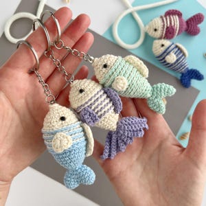May include: Handmade crochet fish keychains in various colors, including blue, purple, and green. Each fish has a unique striped pattern and a silver keychain ring. The keychains are a charming accessory.