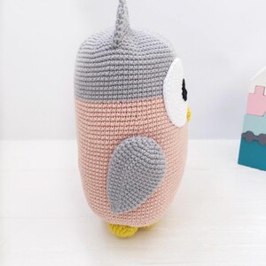 May include: A crocheted owl plush toy with a pink body, gray wings, and a white face with black eyes. The owl has a yellow beak and feet.