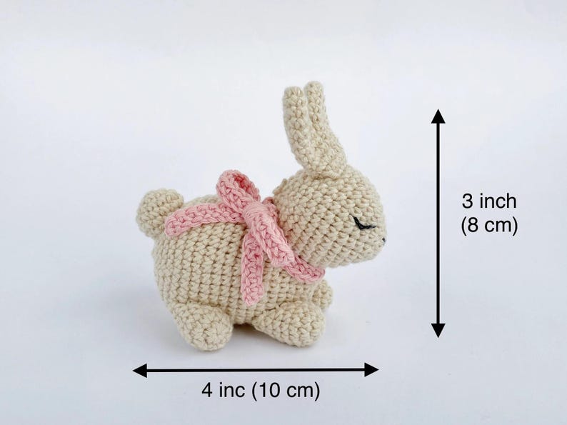 May include: A small crocheted bunny with a pink bow, measuring 3 inches tall and 4 inches wide.