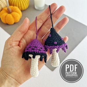 May include: Two crocheted mushroom ornaments. One has a purple cap with black accents, the other has a black cap with purple accents. Both have white stems and hanging strings. The ornaments are handmade and likely for seasonal decor.