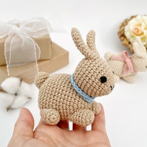 May include: Two crocheted bunny toys. One is beige with a blue collar and the other is white with a pink bow.