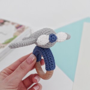 May include: A gray crocheted airplane toy with blue and white accents attached to a wooden teething ring.