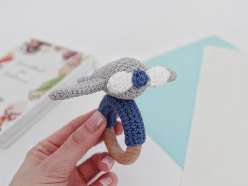 May include: A gray crocheted airplane toy with blue and white accents attached to a wooden teething ring.