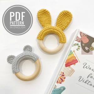 Puede incluir: Dos mordedores para bebés de crochet, uno con orejas de conejo grises y otro con orejas de conejo amarillas. Ambos mordedores están unidos a anillos de madera.