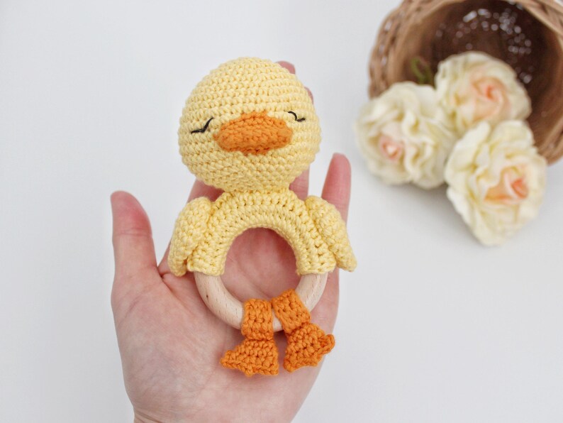 Puede incluir: Un sonajero de beb&eacute; de pato amarillo tejido a crochet con pies naranjas y un anillo de madera.