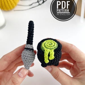 May include: A crochet pattern for a black and gray wand and a black cauldron with a swirling lime green liquid spilling over the rim. The text PDF PATTERN IN ENGLISH is visible in a circular badge. The items are crafted from yarn.