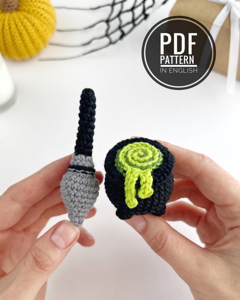 May include: A crochet pattern for a black and gray wand and a black cauldron with a swirling lime green liquid spilling over the rim. The text PDF PATTERN IN ENGLISH is visible in a circular badge. The items are crafted from yarn.