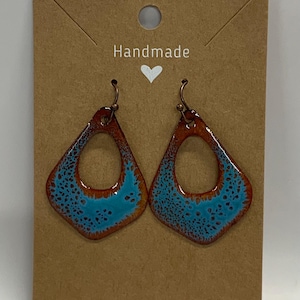 May include: Handmade earrings with a unique design. The earrings feature a diamond shape with a turquoise blue center and a brown border. The earrings are displayed on a brown card with the word "Handmade" and a heart symbol.