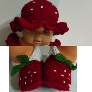 May include: A red crocheted baby outfit, including a hat and booties, designed to resemble a strawberry. The hat has white polka dots and a ruffled brim. The booties are red with white tops and green leaf accents.