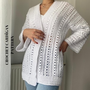 Puede incluir: Un cárdigan blanco de ganchillo con detalles calados y mangas acampanadas. La prenda de manga larga tiene cuello en V y un diseño de tejido abierto texturizado. El texto "CROCHET CARDIGAN PATTERN" está impreso verticalmente.