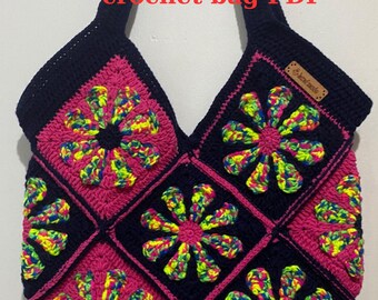 May include: A handmade crochet bag featuring a floral design. The bag is composed of square panels in black, pink, and vibrant neon colors. The text "crochet bag PDF" is visible at the top. A small brown tag is attached to the bag.