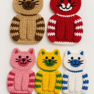 Op de afbeelding: Zes handgemaakte gehaakte kattenapplicaties in verschillende kleuren. De katten hebben zwarte ogen en snorharen en dragen truien met gestreepte of effen ontwerpen. Kleuren zijn onder meer bruin, rood, roze, geel en wit.