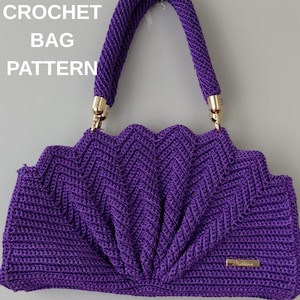Può includere: Una borsa all'uncinetto color viola vivace caratterizzata da una texture a ventaglio smerlata e un manico singolo fissato con finiture in metallo dorato. Il testo CROCHET BAG PATTERN è visibile in alto a sinistra e vi è una piccola etichetta dorata.
