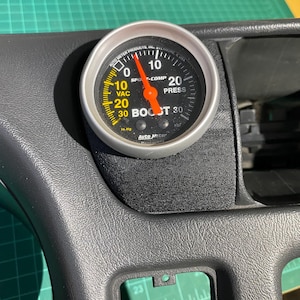 May include: A black and silver boost gauge with a yellow face and a red needle. The gauge reads from 0 to 30 psi and has a vacuum scale from 0 to 30 inHg. The gauge is labelled "Boost" and "Sport-Comp Press".