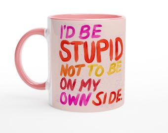 May include: Pink ceramic mug with a pink rim. The mug has a white background with the text "I'd be stupid not to be on my own side." in colorful brushstrokes.