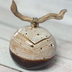 May include: A white ceramic round box with a brown bottom and a driftwood lid. The lid is decorated with a brown and gold wire.