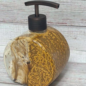 May include: A ceramic soap dispenser with a brown and white leaf pattern. The dispenser has a bronze pump.