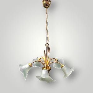 May include: A vintage chandelier with a gold finish and five frosted glass shades shaped like flowers. The fixture hangs from a gold chain and ceiling mount. The design is elegant and decorative.