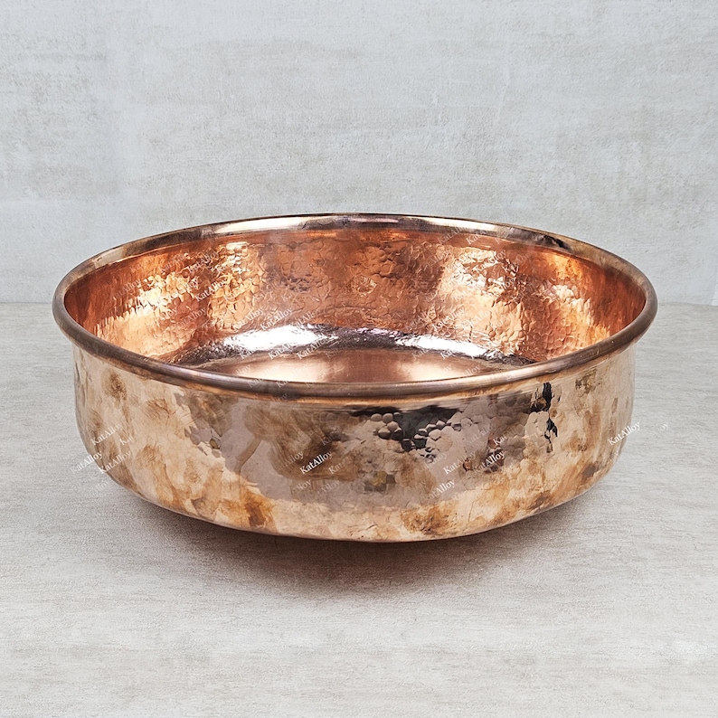 May include: A large, round copper bowl with a hammered finish. The bowl is empty and has a shiny, metallic finish.