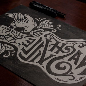 May include: A black and white illustration of a guitar with the words "The Wild" written on it. A bird is perched on top of the guitar.