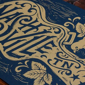 May include: A blue and gold poster with the text "Nashville, TN" in a decorative font. The poster features a stylized key with a bird and leaves.