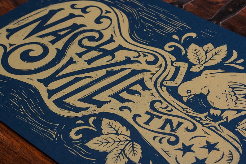 May include: A blue and gold poster with the text "Nashville, TN" in a decorative font. The poster features a stylized key with a bird and leaves.