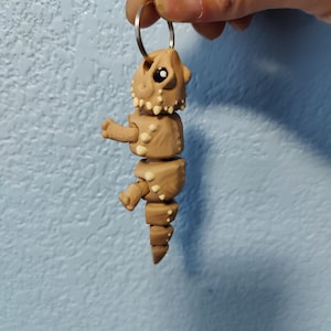 May include: A brown and white segmented dinosaur keychain with a black eye. The dinosaur is attached to a silver key ring.