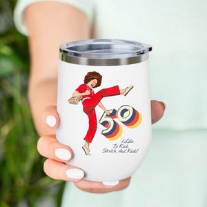 May include: White insulated wine tumbler with a lid, featuring a retro illustration of a woman in a red jumpsuit kicking. The design includes the number "50" and the text "I Like To Kick, Stretch, And Kick!"
