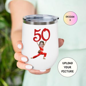 May include: White insulated wine tumbler with a silver rim and lid. The tumbler features a red "50" graphic and a cartoon image of a person holding the number. The text "UPLOAD YOUR PICTURE" is also visible.