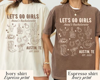 May include: Two t-shirts, one ivory and one espresso, featuring a graphic design for a bachelorette party. The design includes text that reads "LET'S GO GIRLS, Anna's Bachelorette, Austin, TE, EST. 2025" and various illustrations.