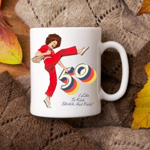 May include: White ceramic mug with a colorful illustration of a woman kicking a large number 50. The text "I Like To Kick, Stretch, And Kick!" is printed below the illustration.