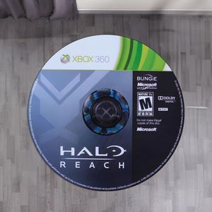 May include: A circular Xbox 360 game disc for Halo Reach. The top section features the Xbox 360 logo and green accents. The lower section is dark blue with the Halo Reach title, Bungie and Microsoft logos, an ESRB Mature 17+ rating, and Dolby Digital text.