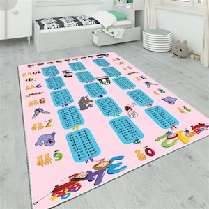 Könnte beinhalten: Ein rosa Kinderteppich mit blauen Einmaleins-Tabellen, Cartoon-Tieren und Zahlen. Der Teppich ist für spielerisches Lernen konzipiert und misst etwa 152 cm x 213 cm.