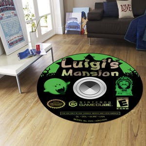 May include: A round black rug featuring the "Luigi's Mansion" video game logo. The rug has a green border with the game's title and characters. The rug is designed to resemble a Nintendo GameCube disc.