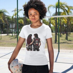 Puede incluir: Camiseta blanca con un estampado gr&aacute;fico de dos personas con chaquetas de cuero negras y pantalones vaqueros rotos. El texto "Justice" est&aacute; impreso en la parte posterior de una de las chaquetas.