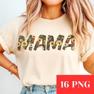 Może przedstawiać: Kremowa koszulka z napisem "MAMA" dużymi literami z kwiatowym wzorem. Kwiatowy wzór przedstawia słoneczniki, czerwone róże i białe kwiaty na ciemnym tle. Koszulka jest noszona przez osobę z blond włosami i złotą biżuterią.