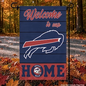 May include: A rectangular garden flag featuring a dark blue background with horizontal lines. The text reads Welcome to our HOME in red and blue lettering. A white outline of a buffalo with a red stripe and a Buffalo Bills helmet logo.
