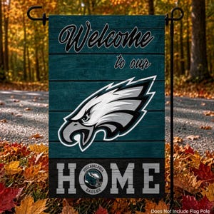 May include: A rectangular garden flag featuring a teal wood-plank background with the text Welcome to our HOME. The Philadelphia Eagles logo is centered in white, black, and silver, with the team name integrated into the letter O in HOME.