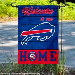 May include: A blue and red garden flag with the text "Welcome to our HOME" and the Buffalo Bills logo. The flag has a wood-grain design and is displayed on a black metal stand.