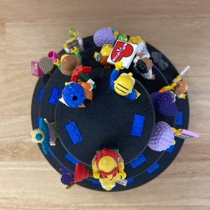 May include: A multi-tiered display stand with a black base and blue trim. The stand is filled with colorful Lego minifigures, including a figure holding a heart-shaped sign.