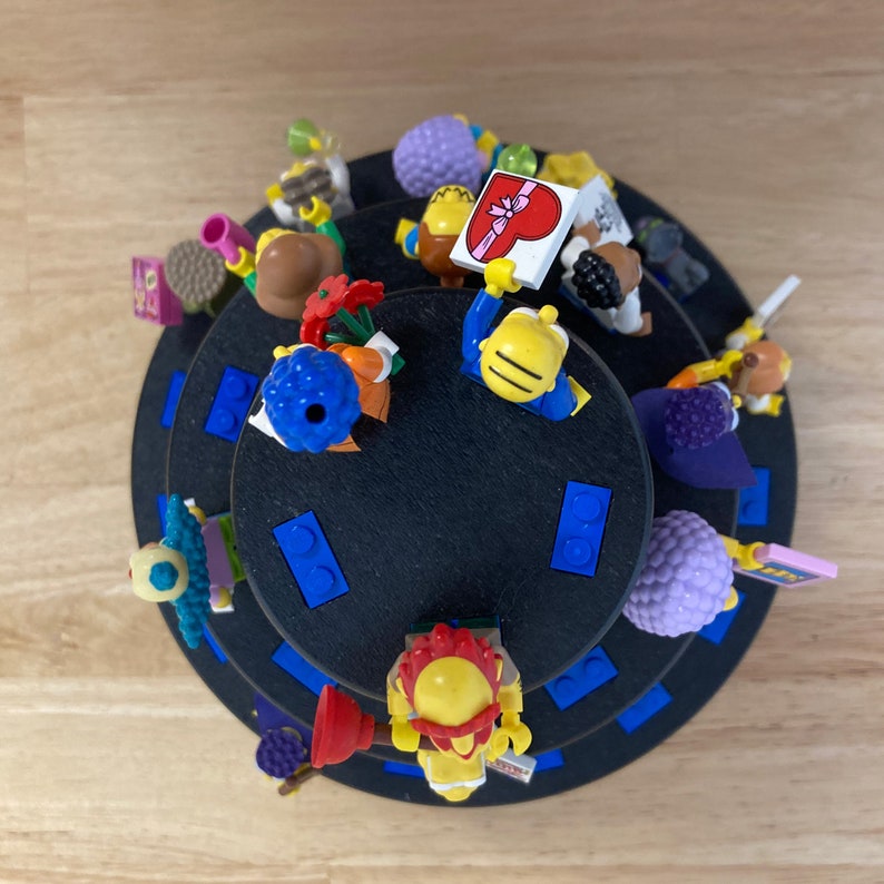 May include: A multi-tiered display stand with a black base and blue trim. The stand is filled with colorful Lego minifigures, including a figure holding a heart-shaped sign.