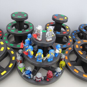 May include: A collection of small, colorful, plastic figurines arranged on a tiered display stand. The figurines are all wearing different colored helmets and have various accessories. The stand is made of black plastic and has a circular base.
