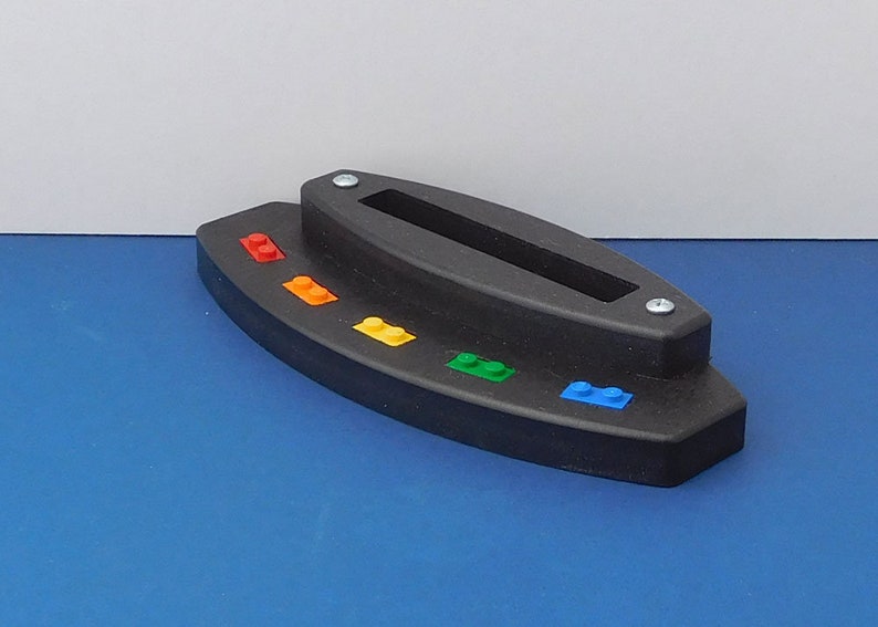 Puede incluir: Un soporte de pl&aacute;stico negro con una ranura para sujetar un tel&eacute;fono u otro dispositivo. El soporte tiene un arco&iacute;ris de peque&ntilde;os ladrillos de pl&aacute;stico unidos a la parte inferior.