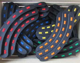May include: A collection of black plastic track pieces with different colored studs. The pieces are curved and have a variety of colors including red, blue, yellow, and orange.
