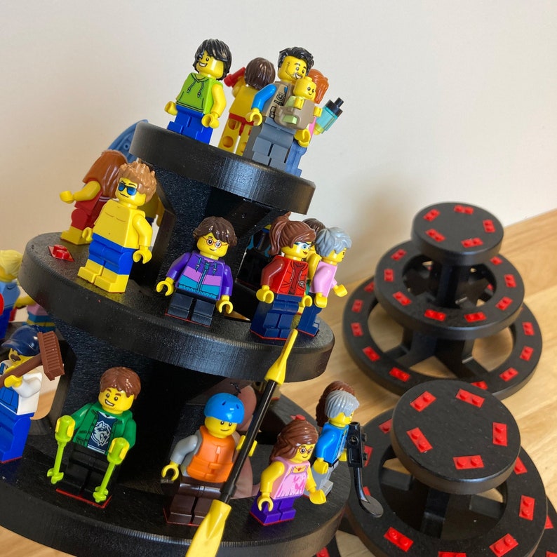 May include: A multi-level display stand with a variety of colorful Lego minifigures. The figures are arranged in a circular pattern on the stand, which is made of black plastic. The stand has three levels, and each level has a different design. The top level has a circular design, the middle level has a square design, and the bottom level has a circular design.